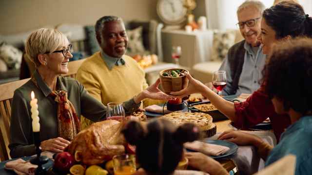 A joyful family gathered around a table for Thanksgiving, sharing food and conversation. The table is adorned with a roasted turkey, pies, and side dishes. Adults and children are smiling, passing a bowl, and enjoying the festive atmosphere in a warmly lit room. 